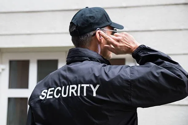 A security officer on an earpiece standing guard at a residence entrance