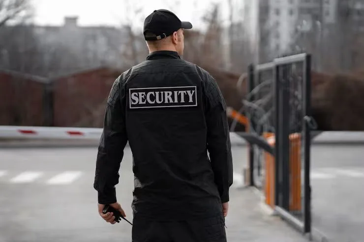 A uniformed security officer posted at a secured gated entrance
